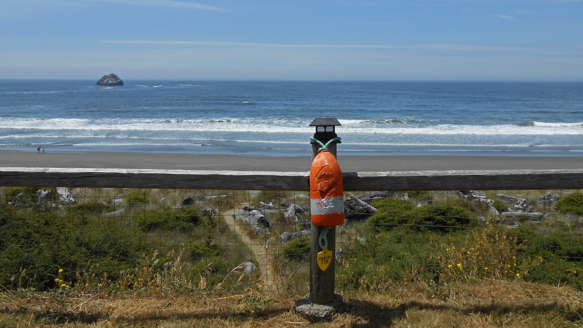 Orange buoy marker on fence post with ocean view